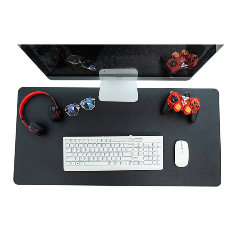 A black leather desk mat with a white keyboard and mouse on top, along with a pair of red headphones and a game controller on a desk.